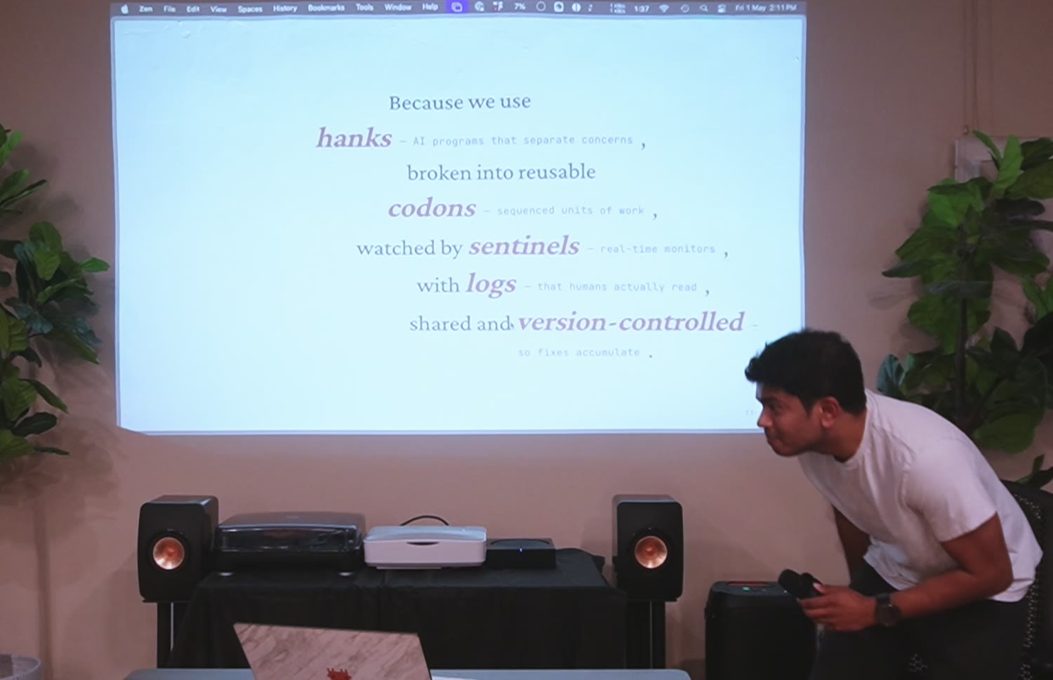 Mid-talk, leaning toward the projected slide listing hanks, codons, sentinels, logs, and version control.