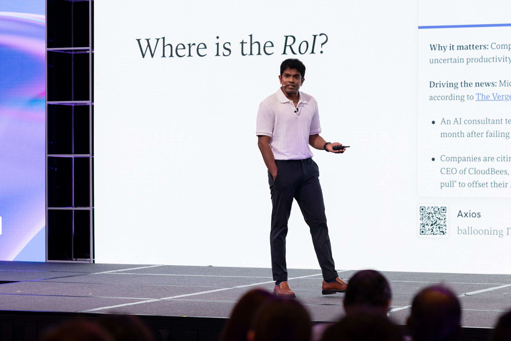 Wide stage shot from the talk. The screen behind reads "Where is the RoI?" with the Axios "ballooning IT costs" snippet visible on the right. I'm at the front of the stage, gesturing with the clicker, the audience silhouetted in the foreground.